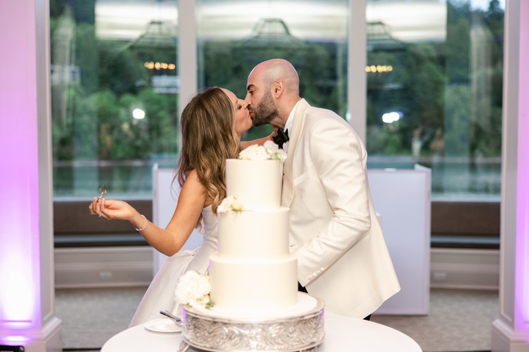 Bride and groom kissing behind their wedding cake